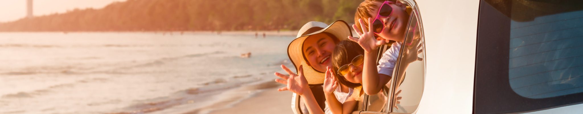 Happy family young woman with her daughter and son sitting in white car with hand up and look out from windows on the beach. Family holiday travel concept.